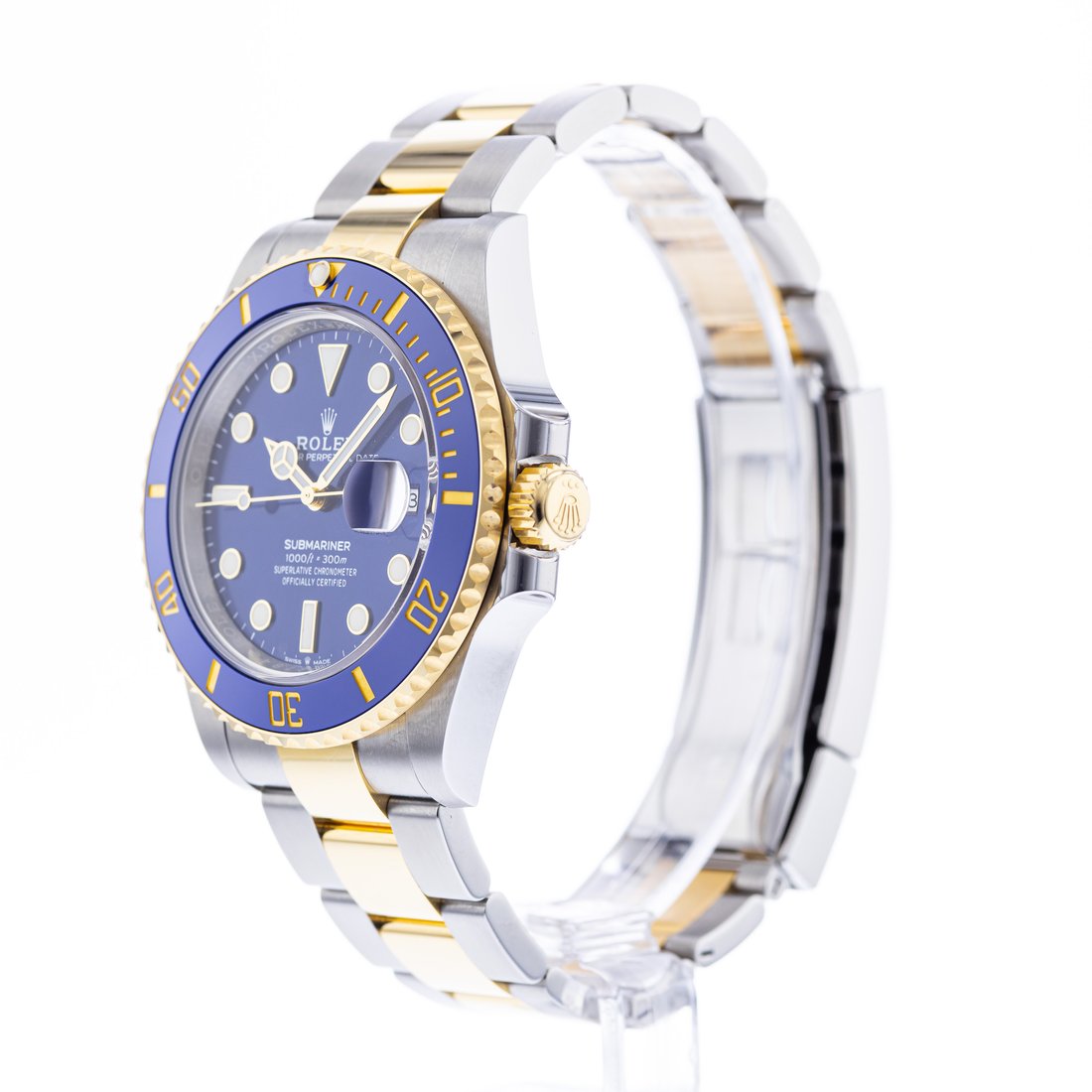 Fluted gold-tone crown at three between guards, brushed case flank, watch on a clear stand